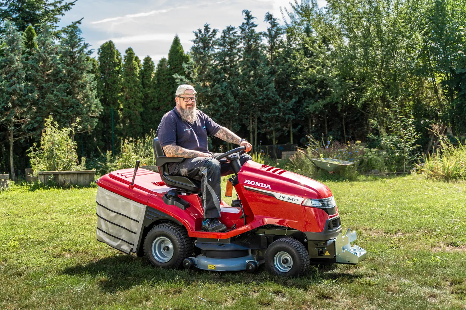 Hausmeister mit Bart fährt auf einem roten Aufsitzrasenmäher über eine gepflegte Wiese.