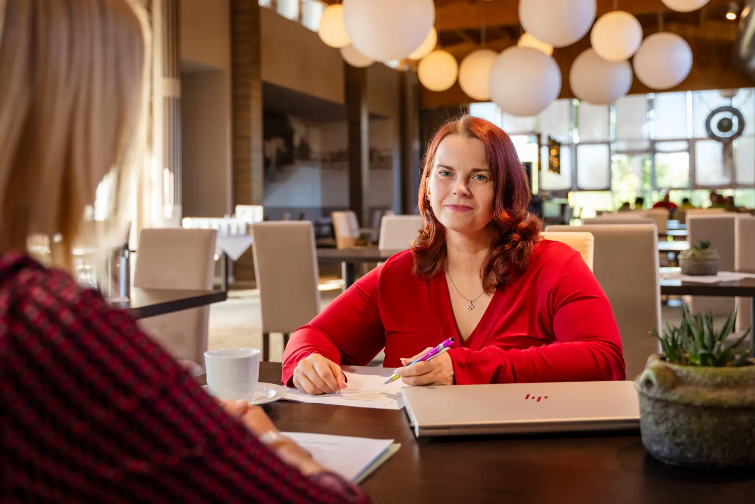 Frau in roter Bluse führt in einem Restaurant ein Gespräch und lächelt in Richtung Kamera.