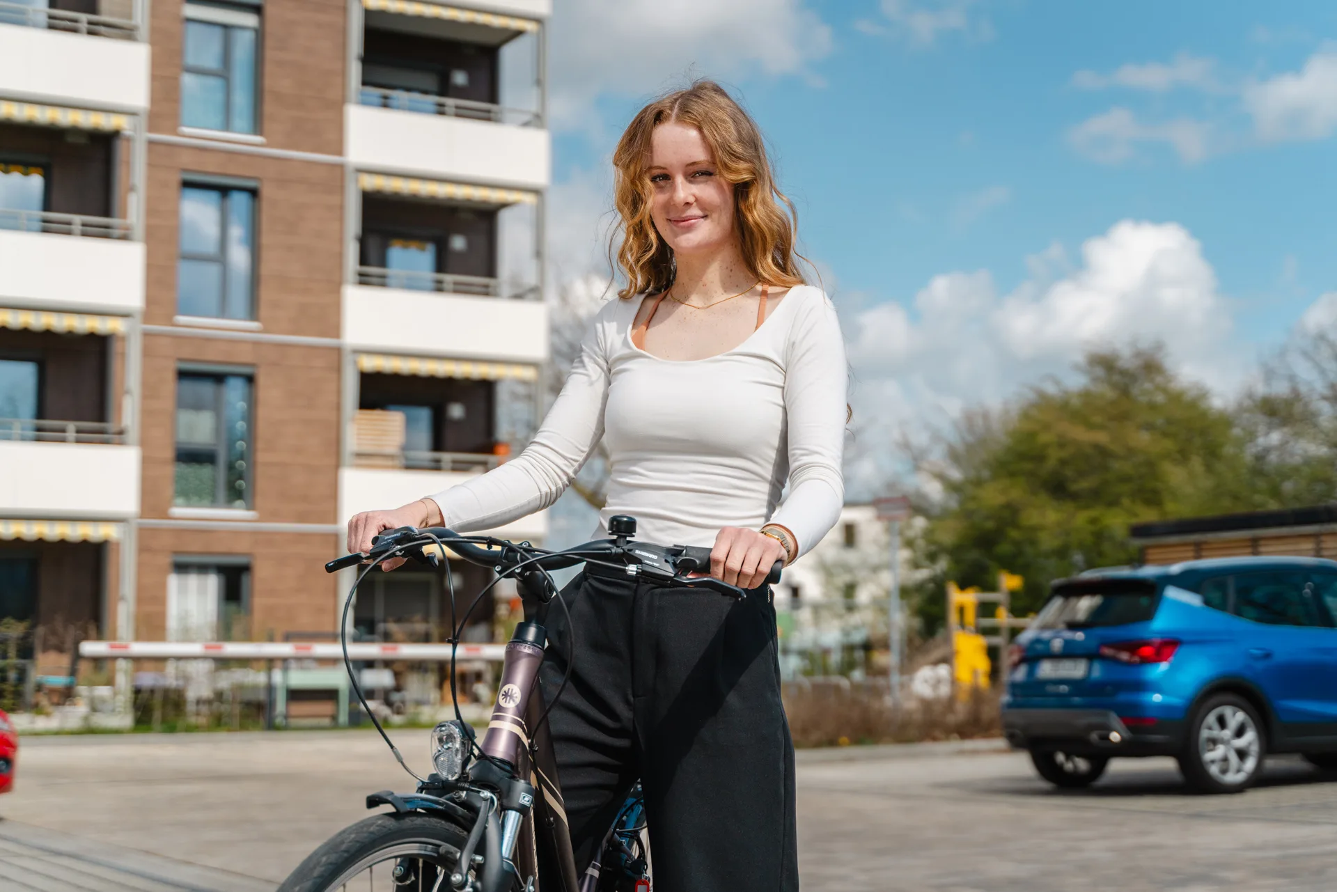 Junge Frau steht mit einem Firmenrad vor einem Gebäude