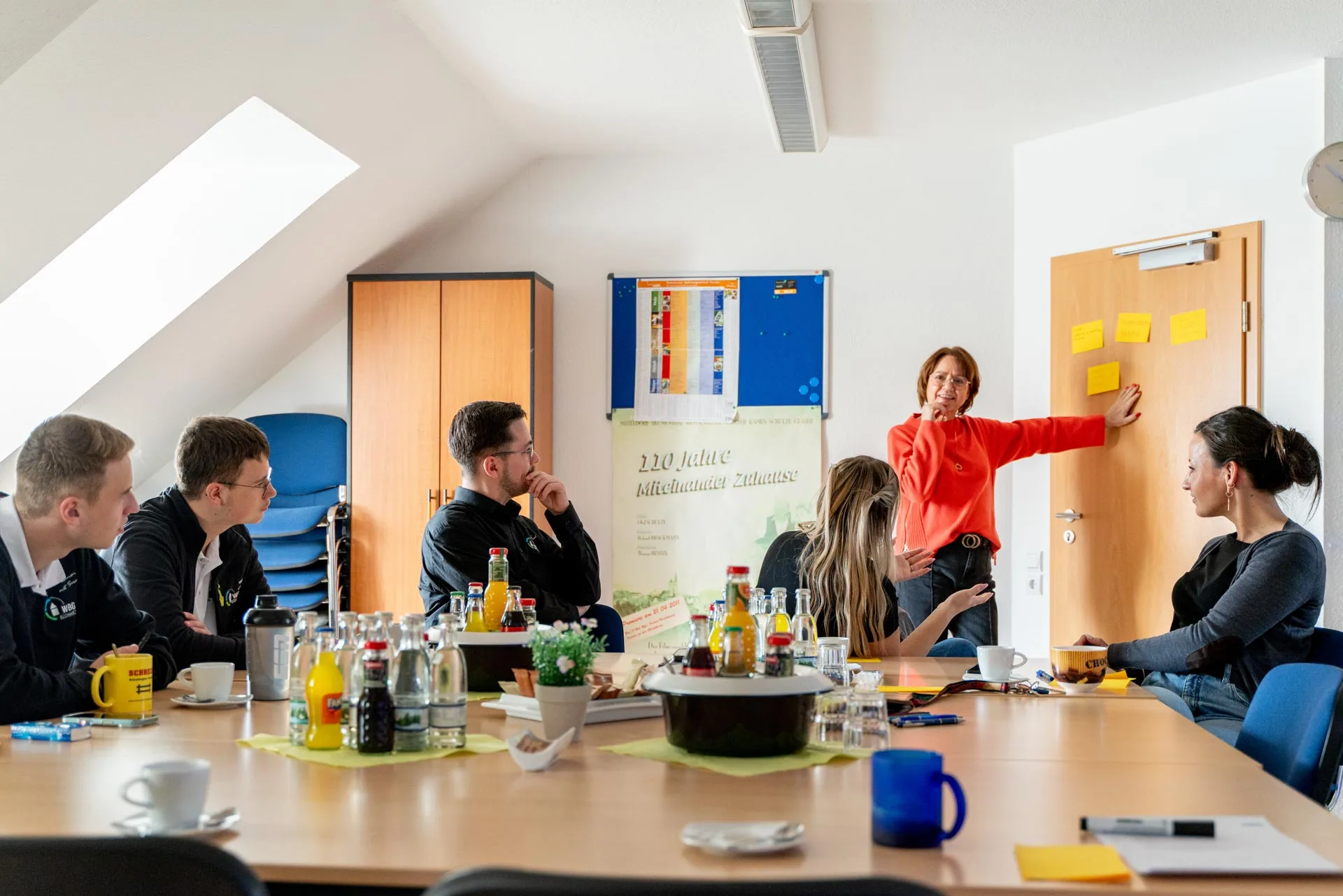 Gruppe junger Menschen sitzt im Seminarraum und hört Iris Palme zu, die an der Tür ein Thema erklärt.