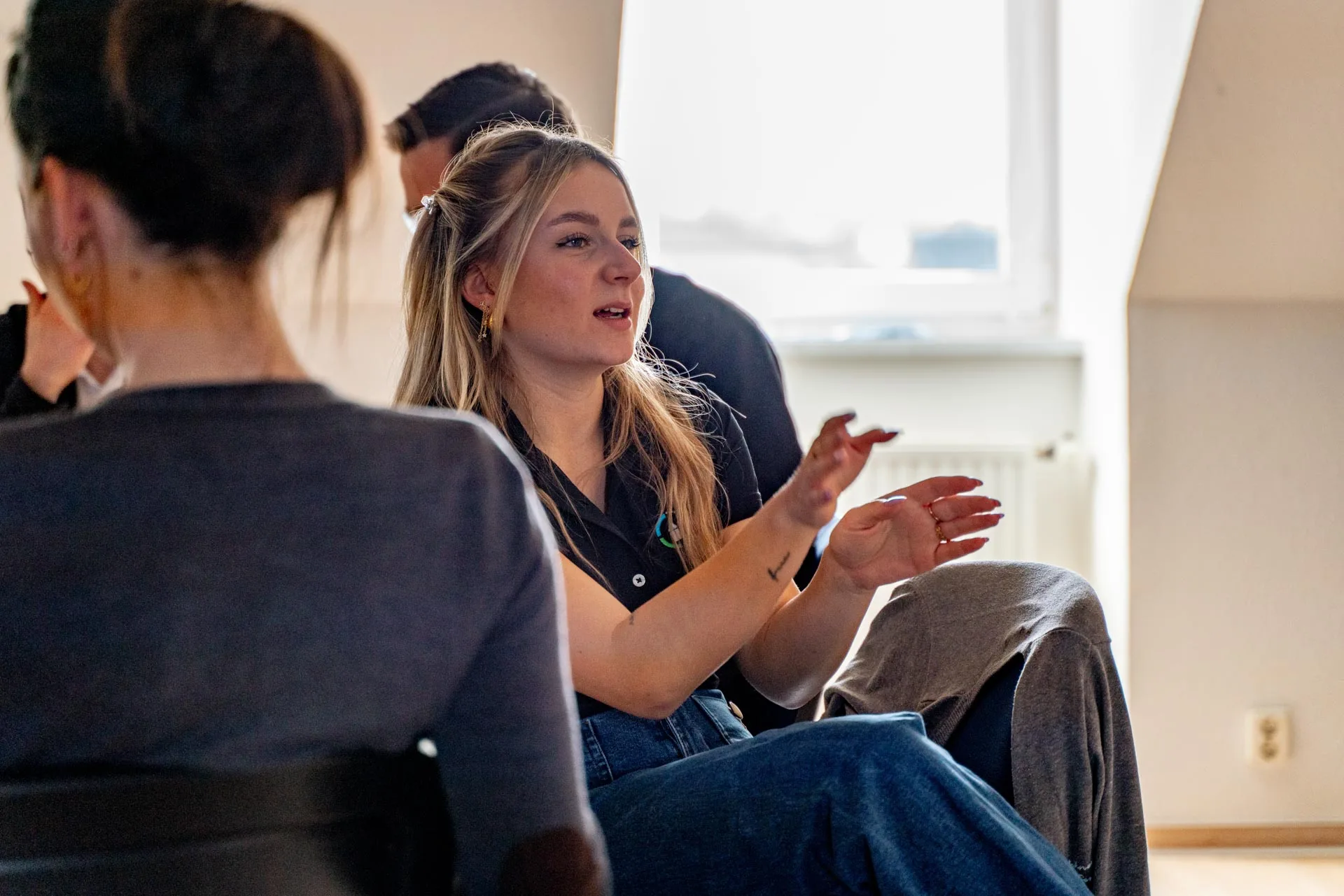 Junge Frau beteiligt sich aktiv an einer Gruppendiskussion in einem hellen Raum.