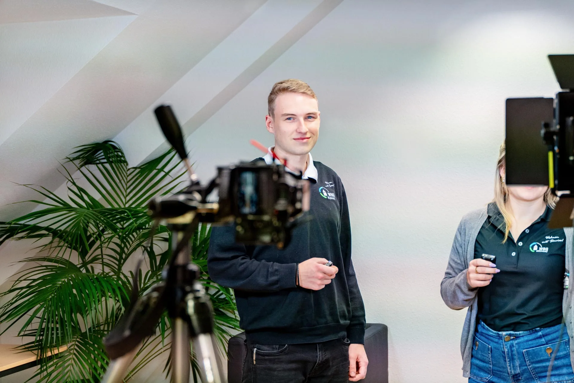 Zwei junge Mitarbeitende bereiten sich vor der Kamera und Beleuchtung auf eine Videoaufnahme vor.