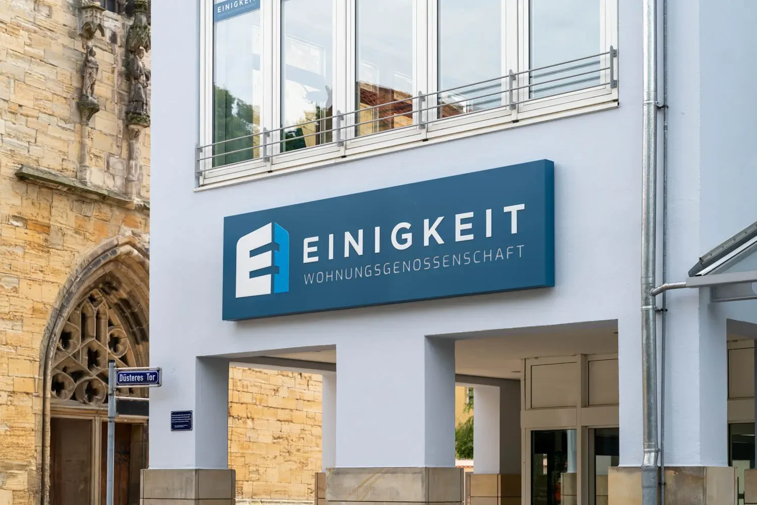 Gebäude mit großem Schild der Einigkeit Wohnungsgenossenschaft neben der Kirche am Düsteren Tor.